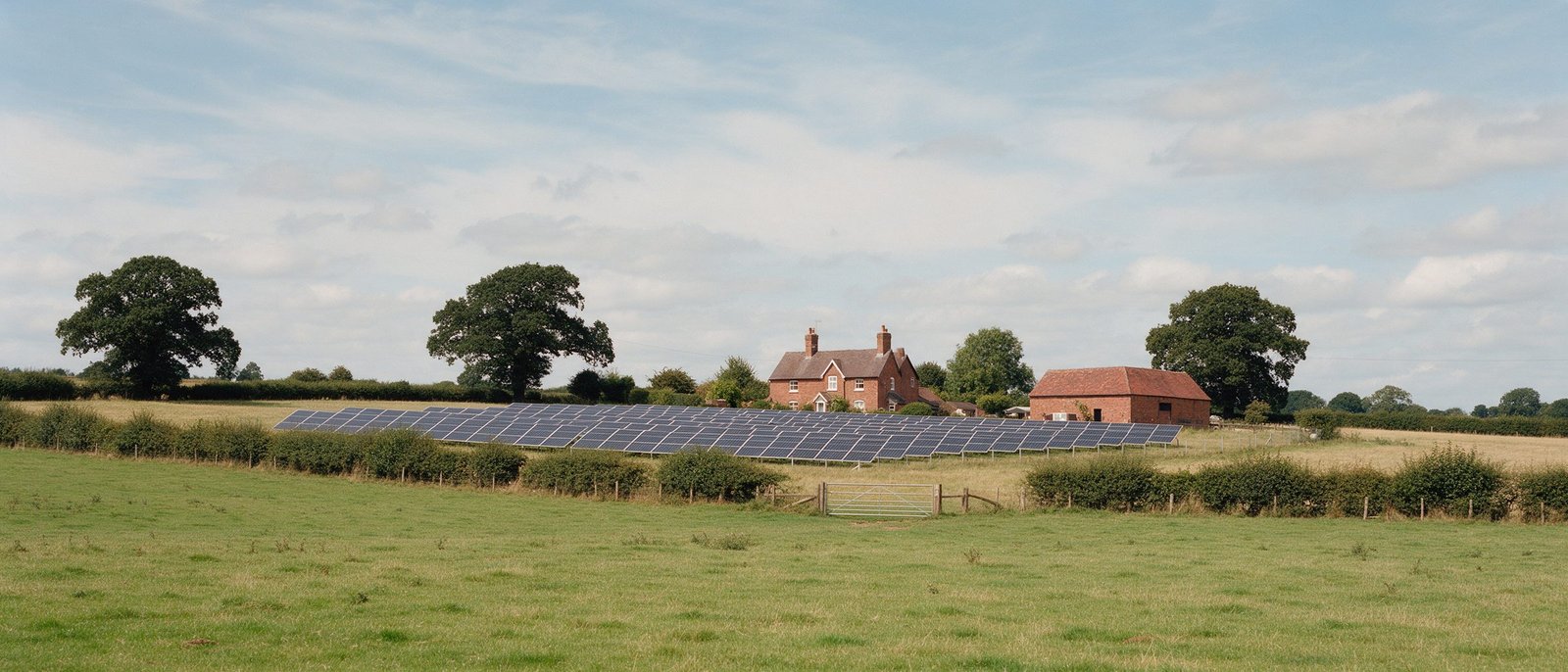Farmland with a solar array in front of a red-brick farmhouse and barn