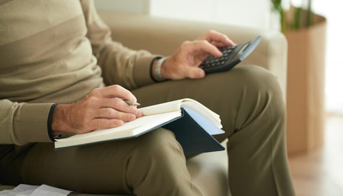Man reviewing pension figures with a notebook and calculator at home